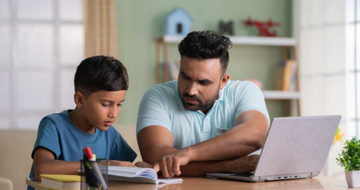 Man working on computer while pointing at child's notebook