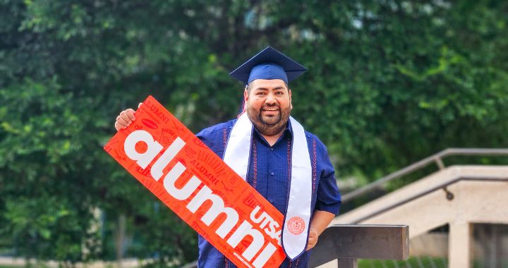 Roger Ruiz holding a "UTSA Alumni" banner