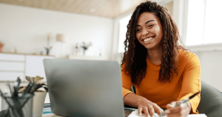 Woman smiling and writing while looking at a computer